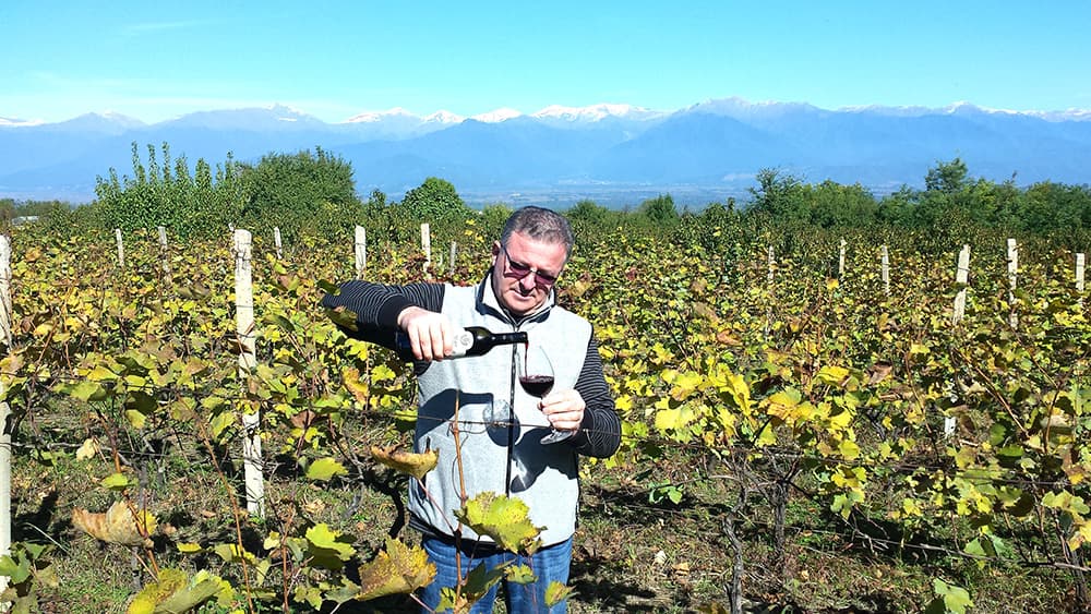 雪をいただくコーカサス山脈を背に、ムクザニの畑でワインを注ぐMUKADO WINESのワインメーカー、ラド・ウズナシュヴィリ